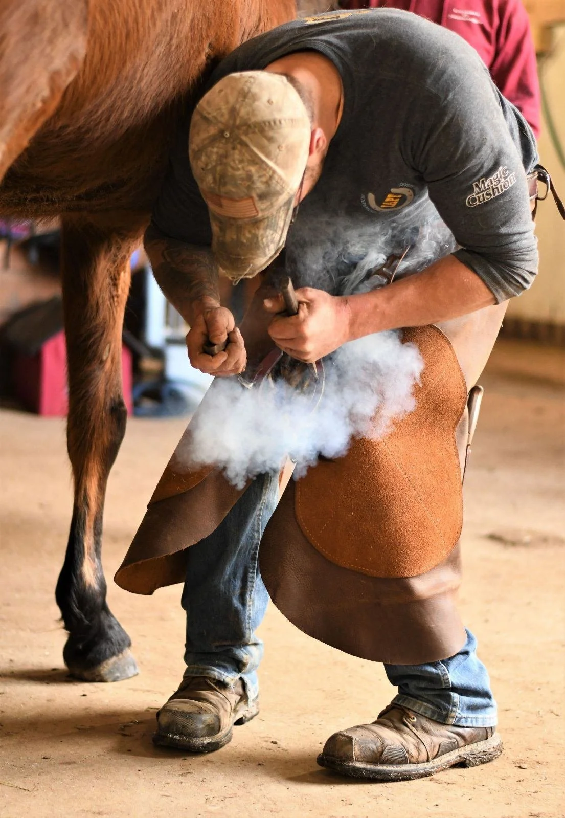 Farrier shaping the hoof of a horse while using a hammer and chisel, with smoke around the hoof.