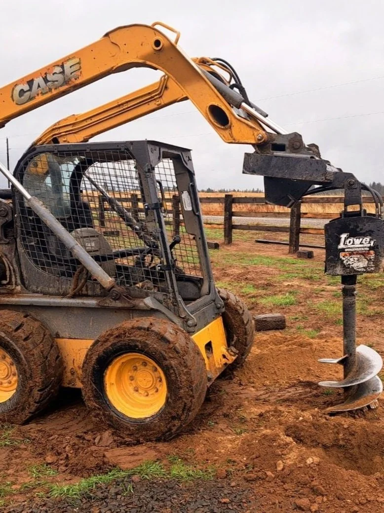 A yellow and black CASE skid-steer loader with muddy tires, digging into the dirt next to an auger attachment.
