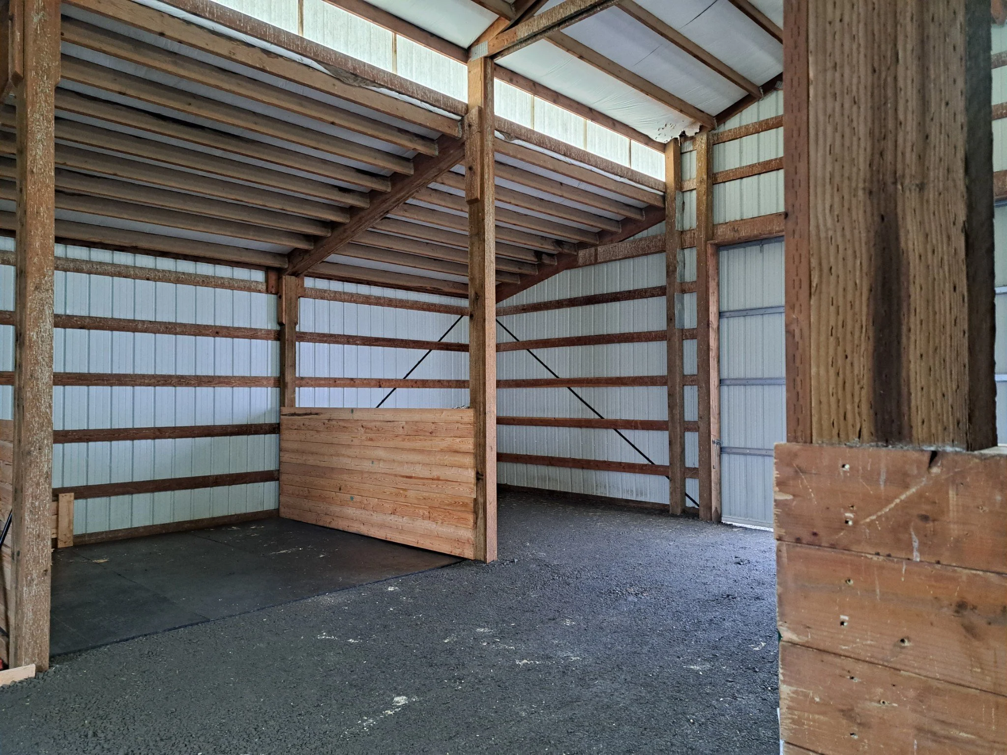 Interior of a wooden structure under construction with vertical and horizontal wooden beams, corrugated metal walls, and a dirt floor.