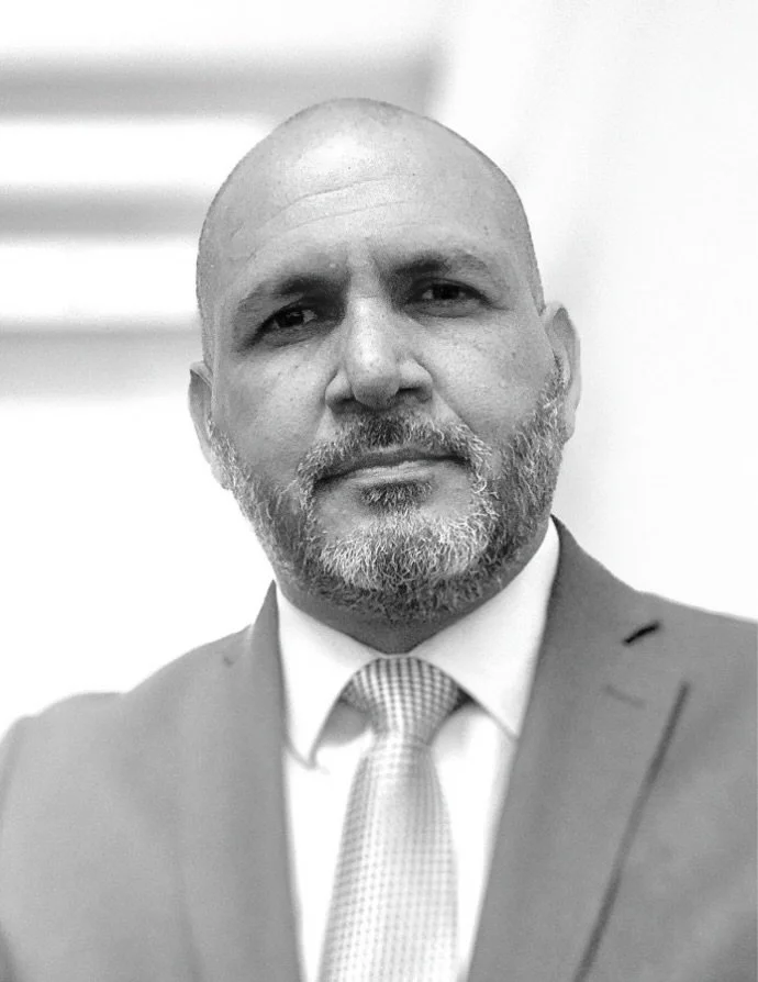 Retrato en blanco y negro de un hombre con barba, barba canosa, con un traje y corbata, en un fondo difuso.