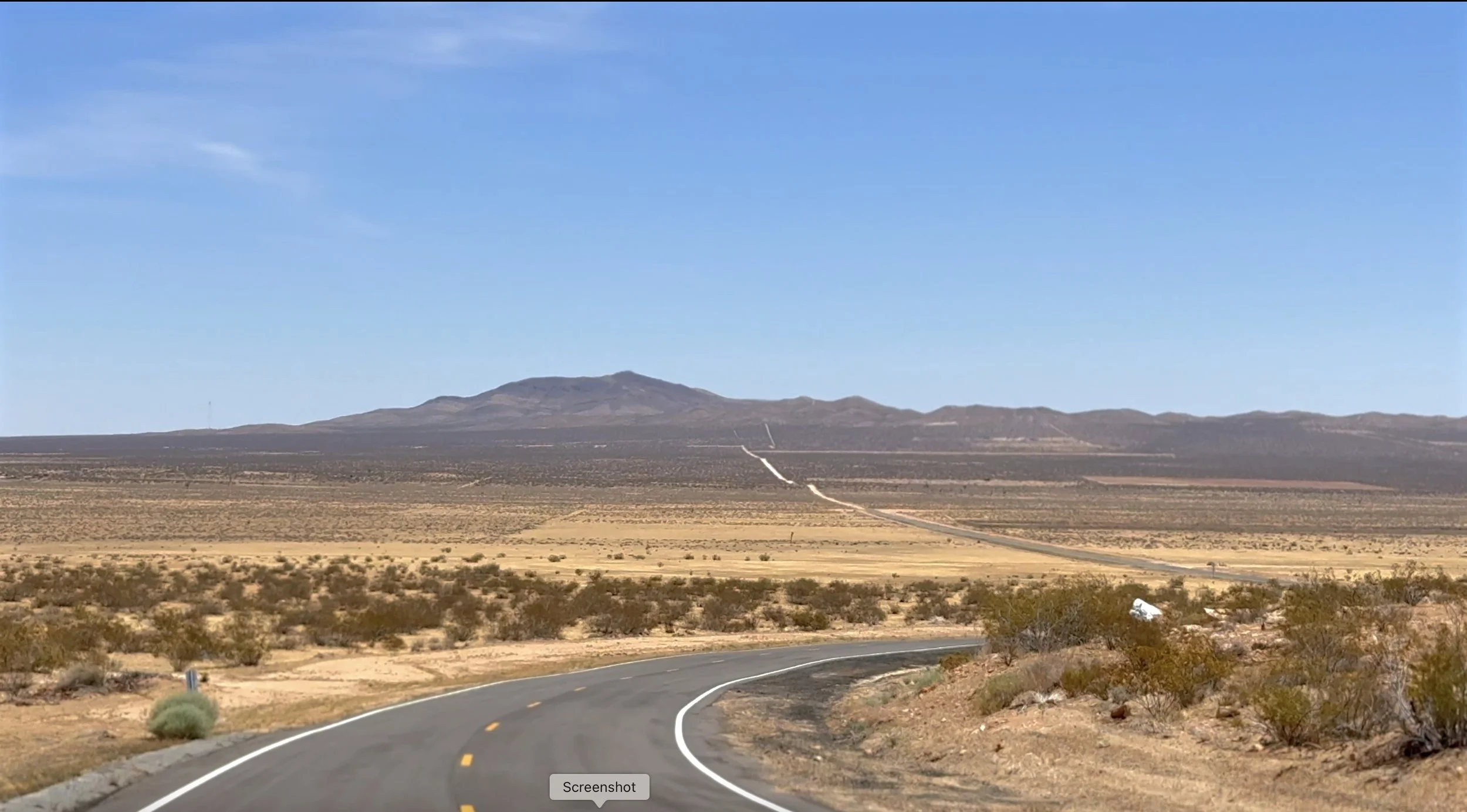 A winding highway running through a desert landscape with sparse vegetation, leading towards distant mountains under a clear blue sky.