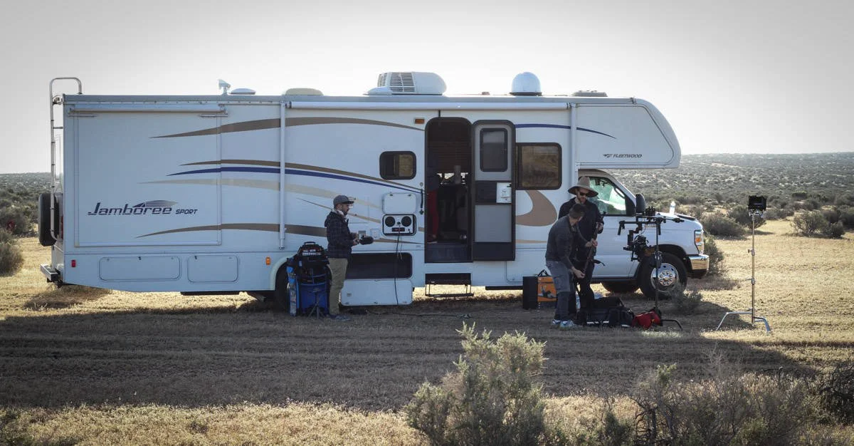 Filmmaking crew shooting in a desert with a white RV and equipment