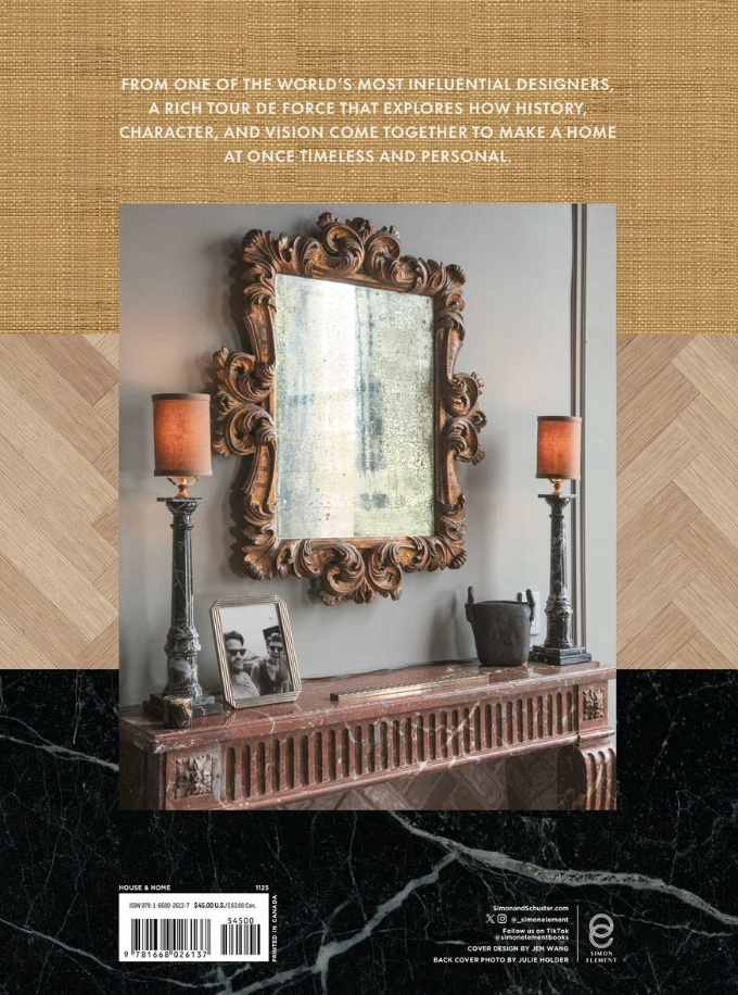 Decorative interior scene featuring an ornate gold mirror, two tall black lamps with orange shades, a black pot, and black-and-white framed photograph, all placed on a red marble fireplace mantel.