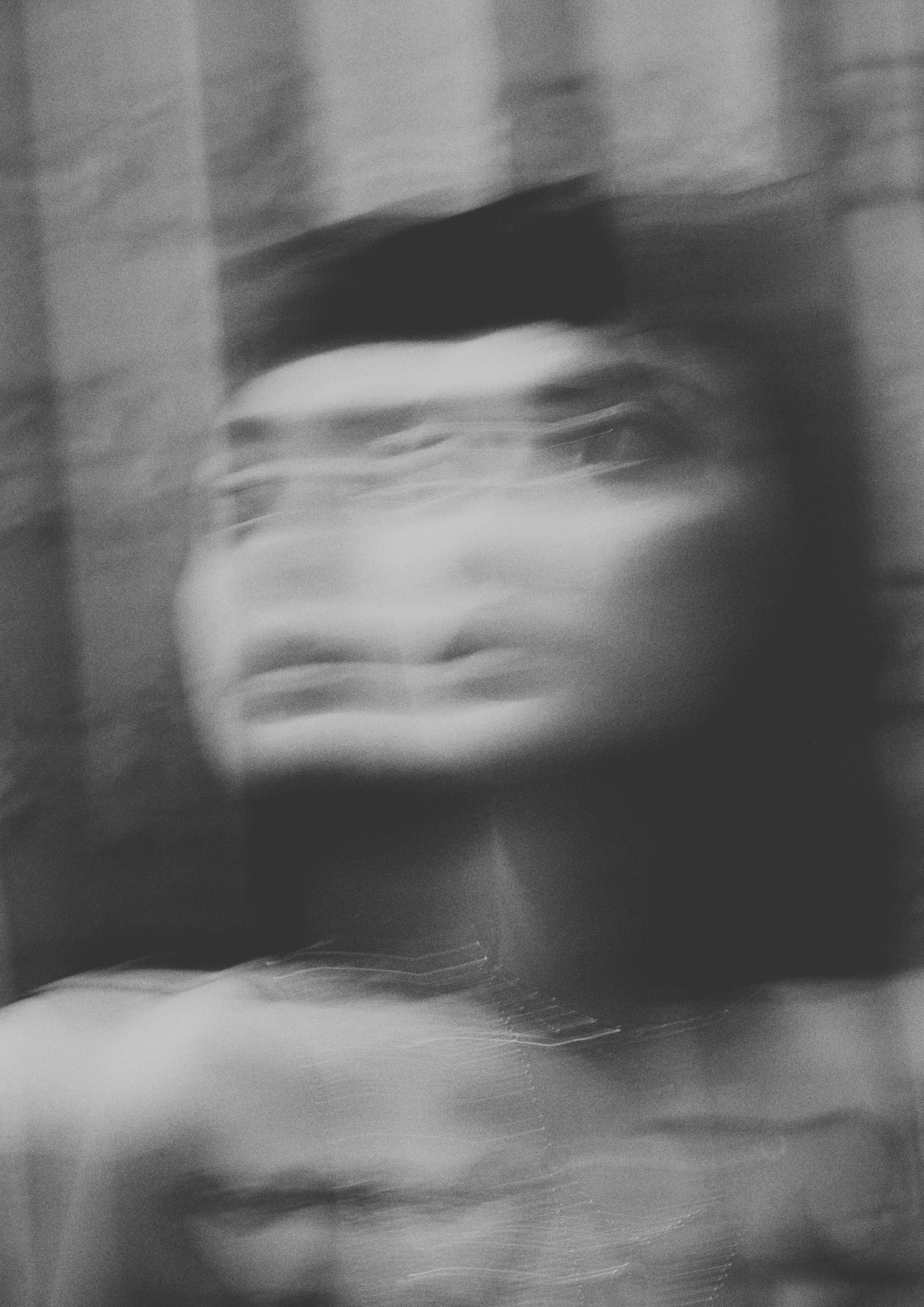 Blurry, abstract black and white photo of a person's face with glasses, creating an artistic, ghostly effect.