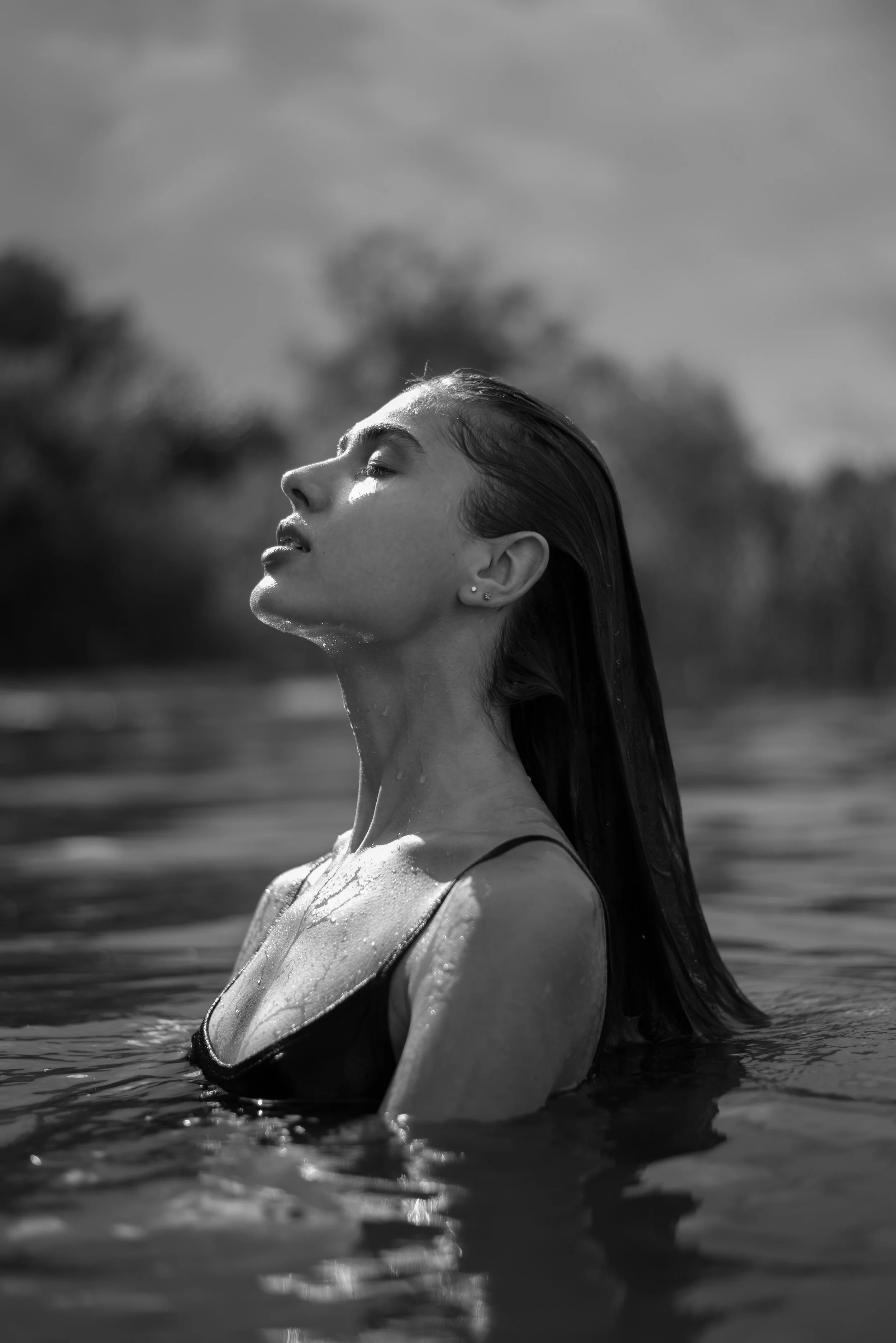 Black and white photo of a woman with wet hair in water with her eyes closed, head tilted back, and water droplets on her face and shoulders.