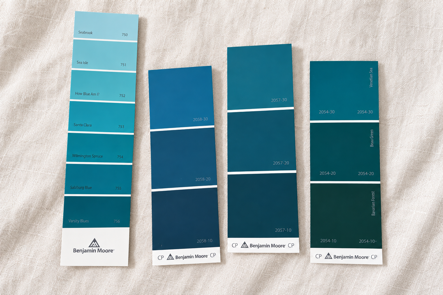 Color swatch cards labeled with paint names and codes, featuring Benjamin Moore branding, arranged on a fabric surface.