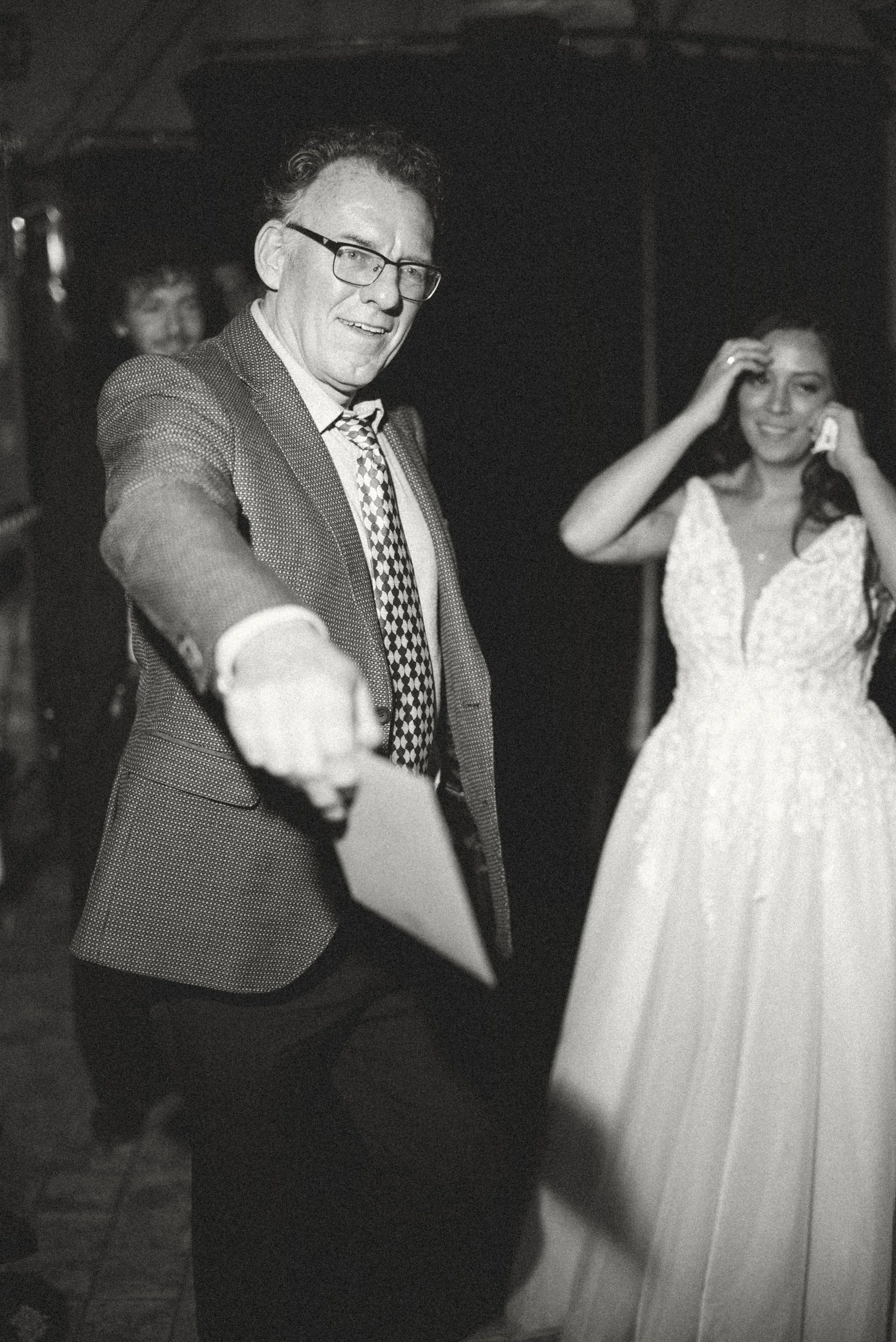 Zwart-witfoto van een lachende man met bril en stropdas, naast een vrouw tijdens een evenement.