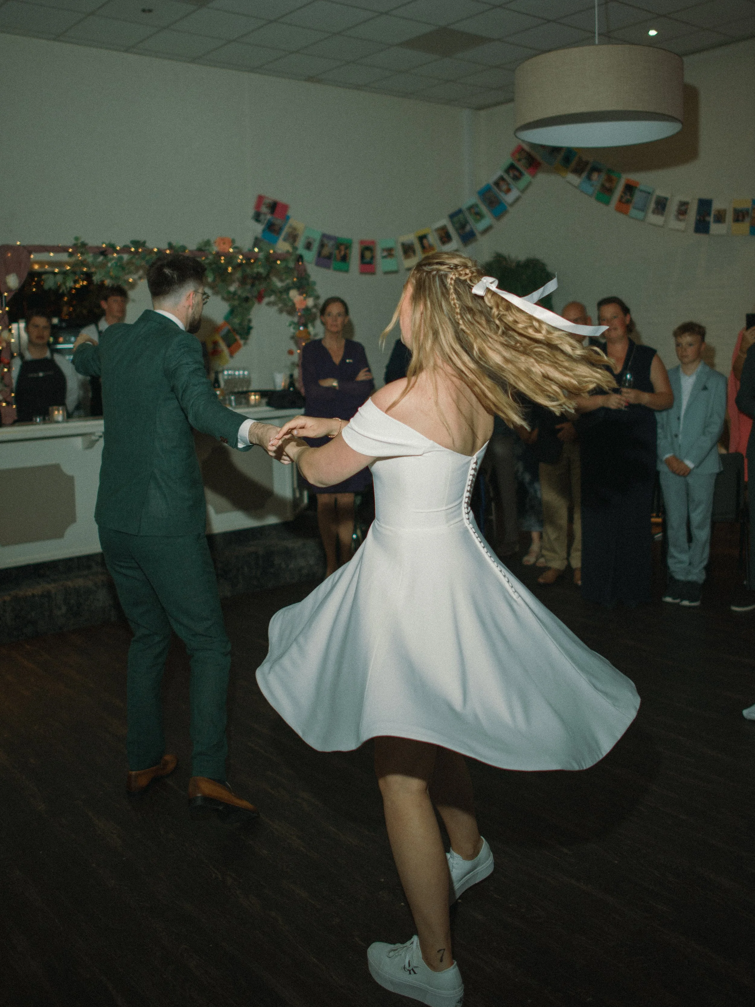Bruidskoppel danst tijdens een feest, omringd door gasten en feestelijke decoratie-trouwfotograaf-assen-groningen-drenthe