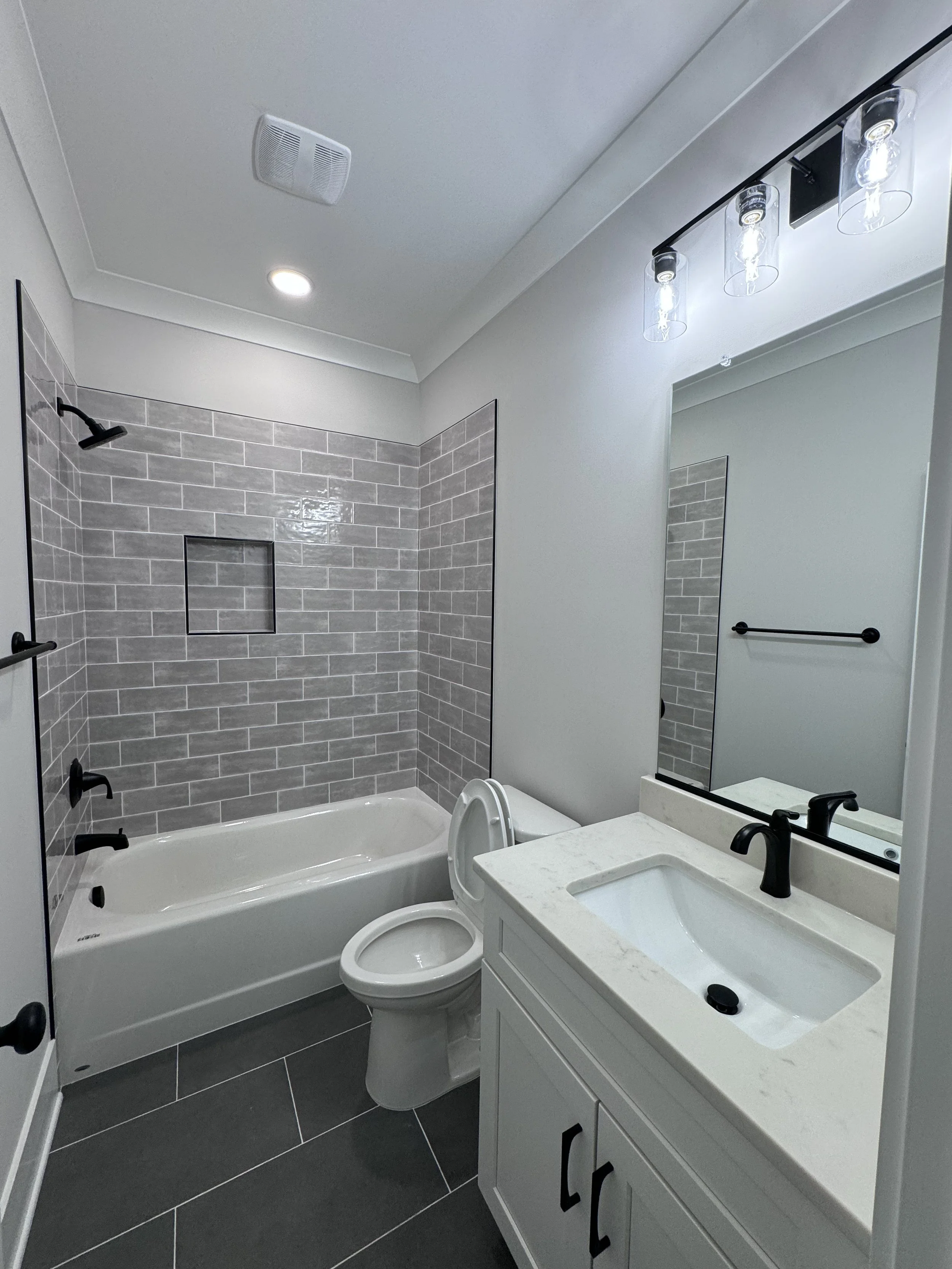 Bathroom with a bathtub, toilet, mirror, sink, and tile walls and floor.