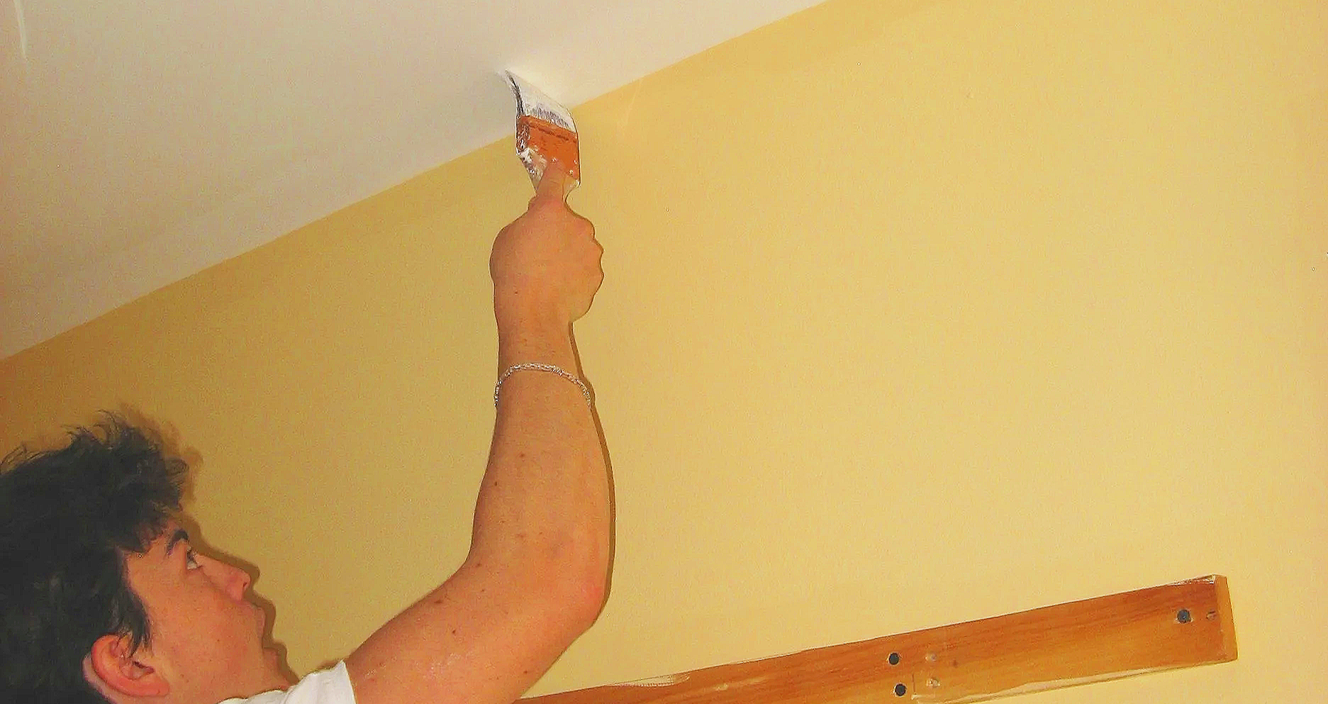 A man painting a wall with a two and a half inch paintbrush.