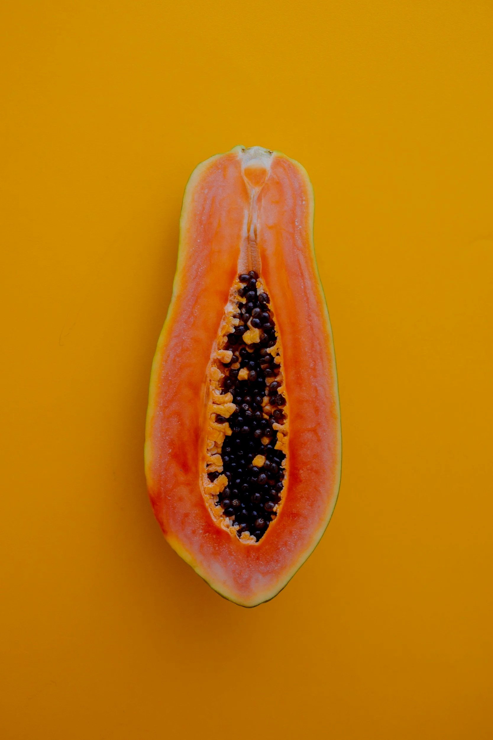 Half of a ripe papaya fruit with orange flesh and black seeds against a yellow background.