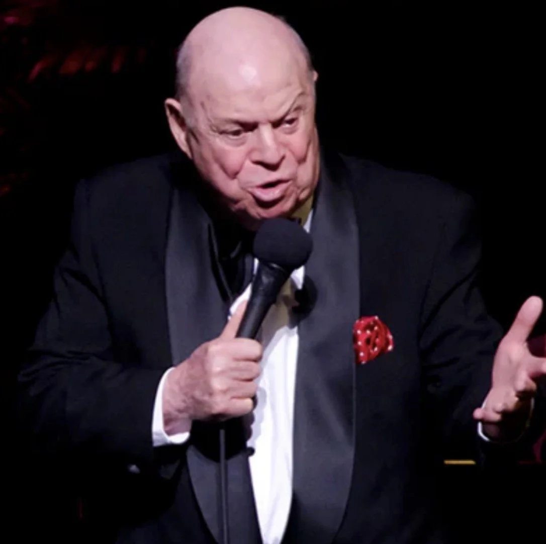 Don Rickles performing in a tuxedo during his peak years as a stand-up comedian known for sharp insult humor.