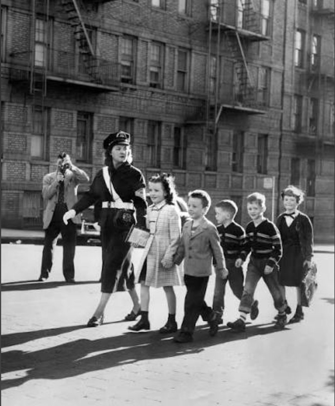 Children serving as school safety patrol members guiding classmates across a city street