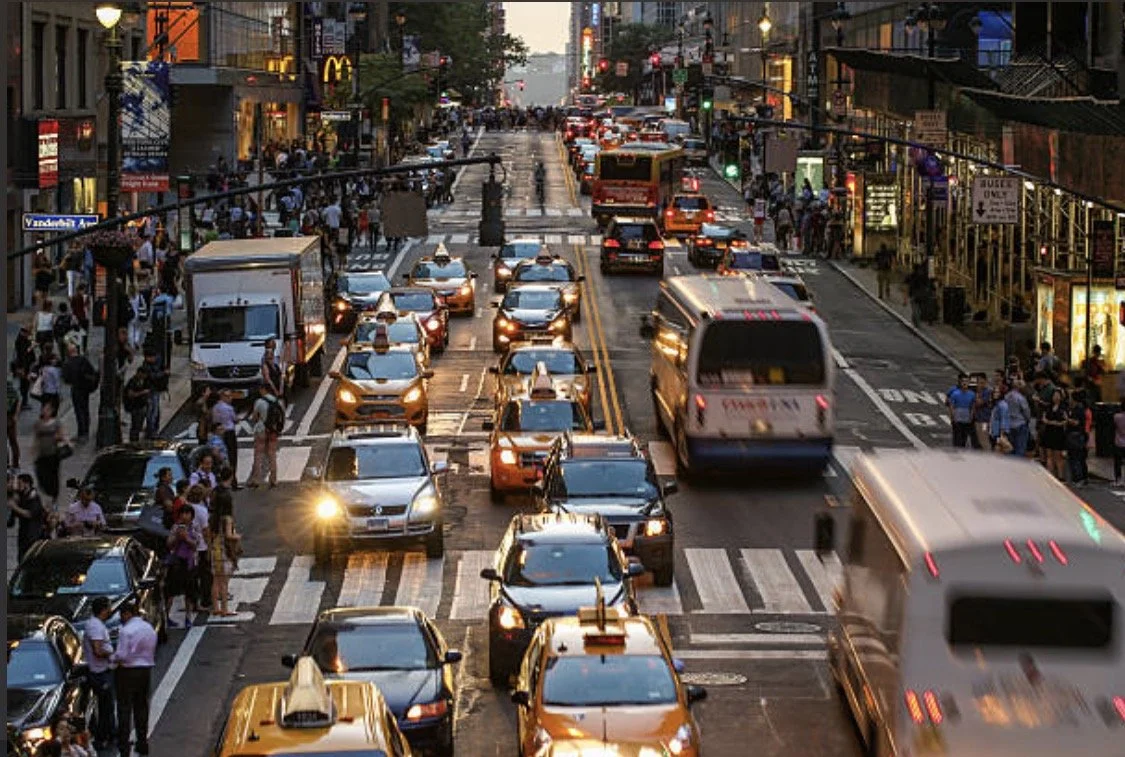 Busy New York street with cars, cyclists, buses, and pedestrians sharing limited space