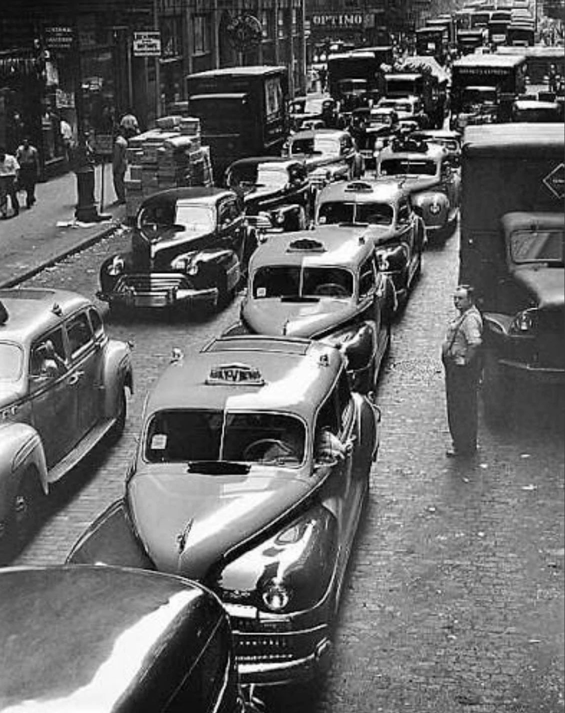Hack cars moving in a single direction along a busy Manhattan avenue lined with tall buildings
