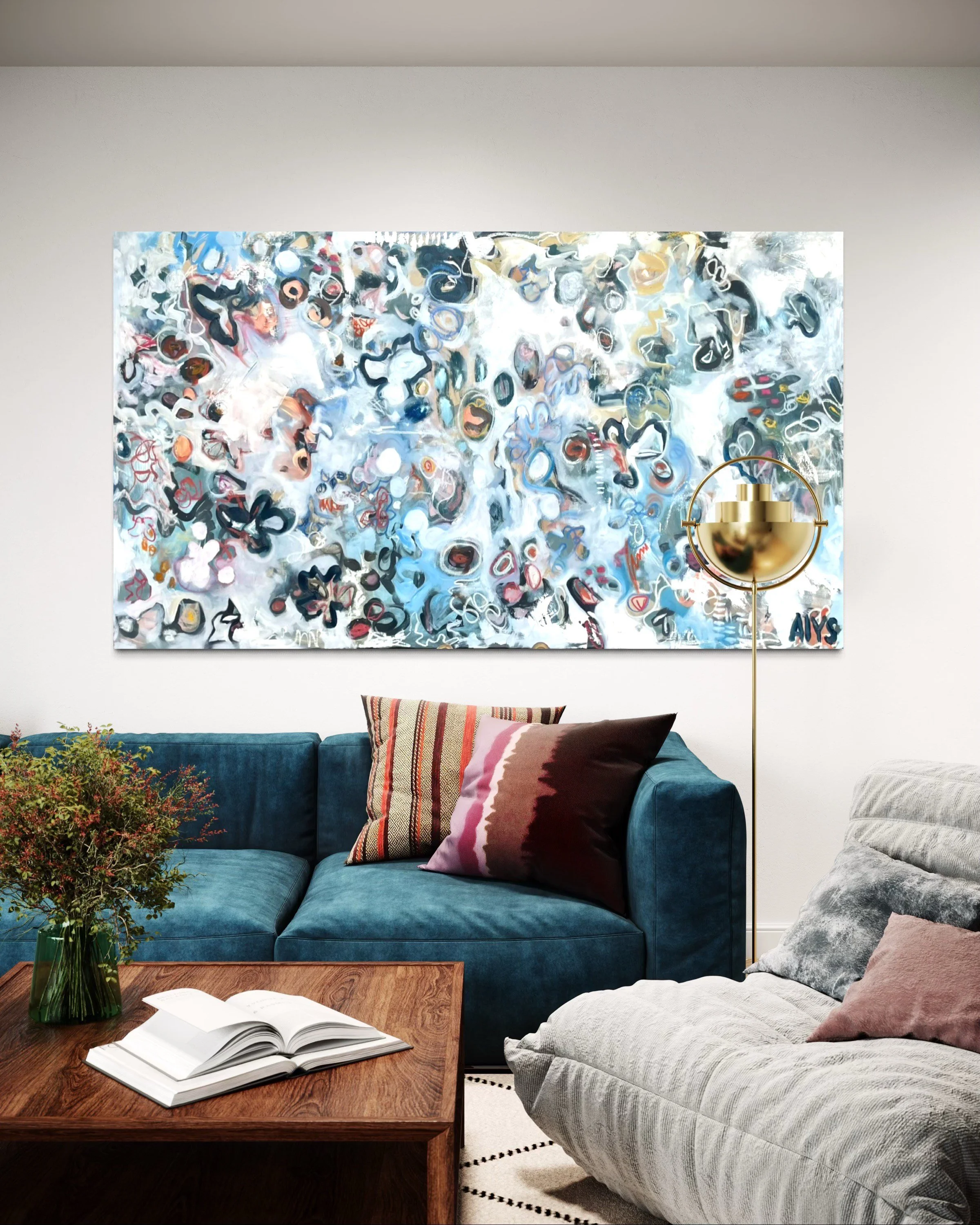 Living room with abstract painting on white wall, blue velvet sofa with patterned pillows, wooden coffee table with book, gray armchair with pink pillow, standing lamp with gold shade, and a vase with green and red flowers.