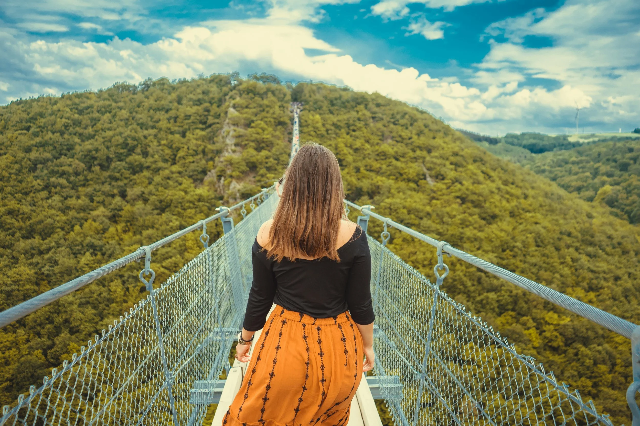 A woman crossing a suspension bridge through forest, representing the trust and perceived integrity required to navigate negotiation and long-term relationships, The Cyr Method