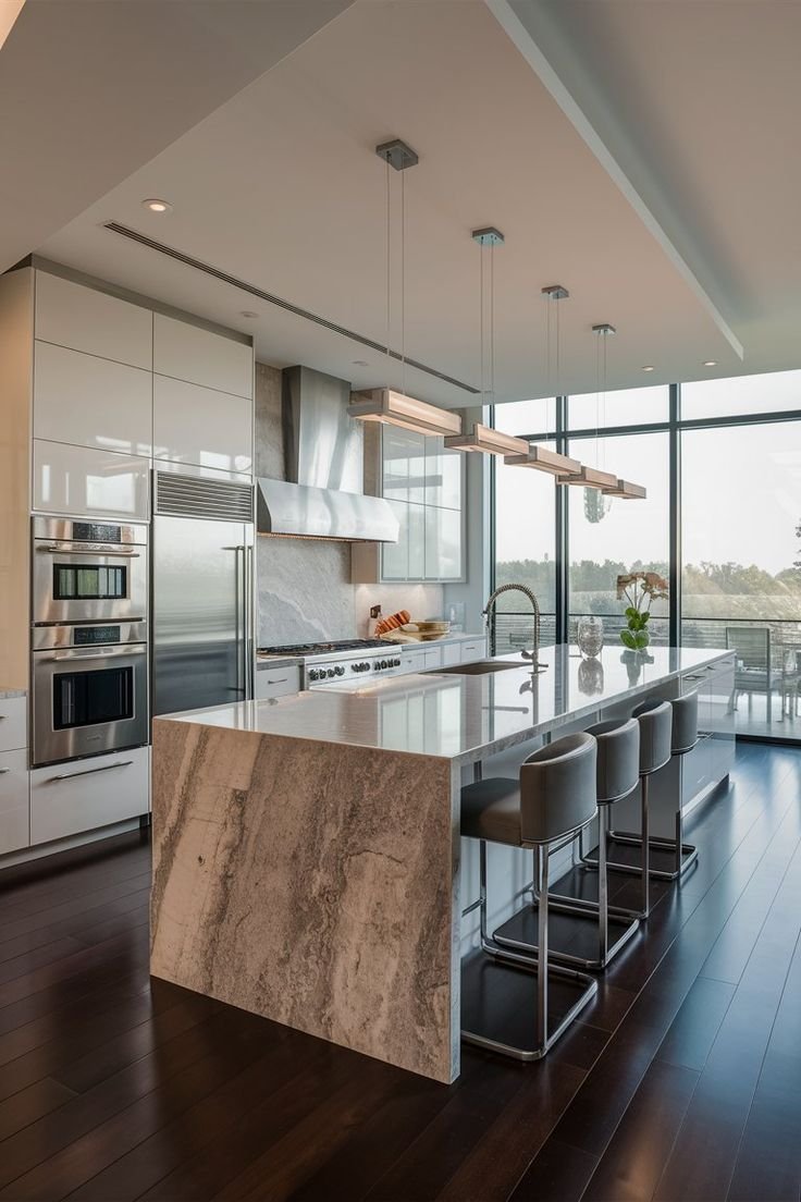 Modern kitchen with white cabinetry, marble island, stainless steel appliances, and large windows with a view outside.