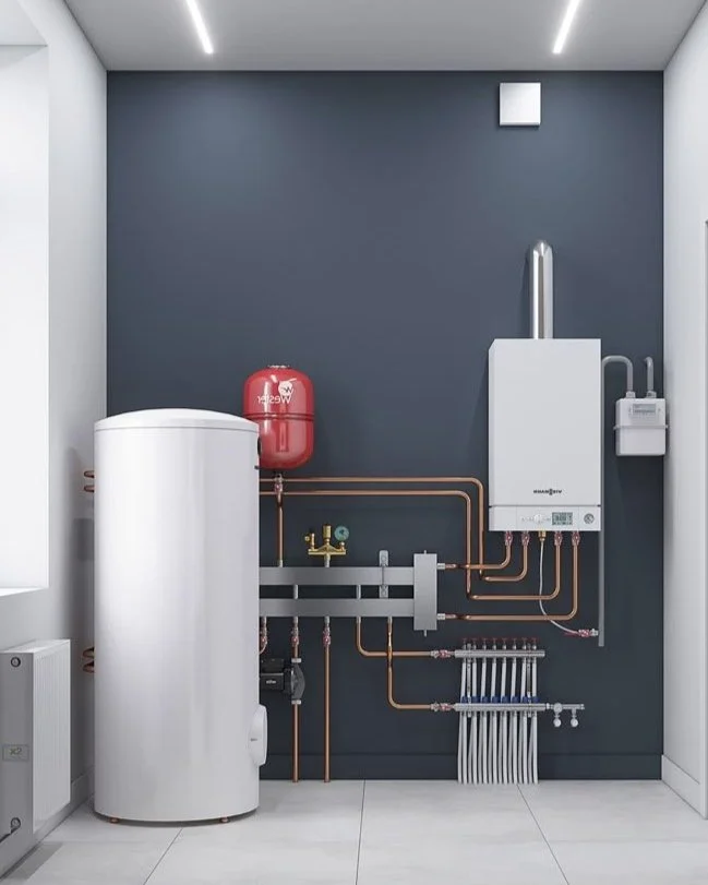 Utility room with water heater, expansion tank, pipes, and heating system components against a dark blue wall.