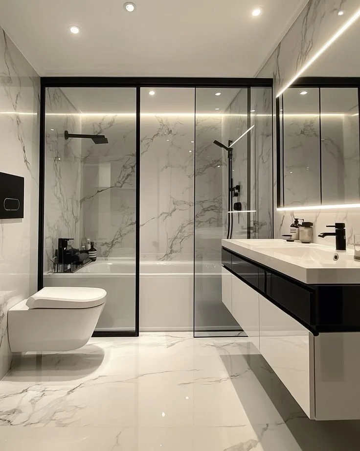 Modern bathroom with marble walls and floor, glass shower enclosure, wall-mounted toilet, black and white vanity with sink, and black fixtures.