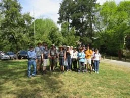 Group of people standing outdoors in a park with trees and cars in the background.