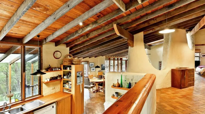 Interior view of a cozy kitchen and dining area with wooden ceiling beams, a large window, and rustic decor.