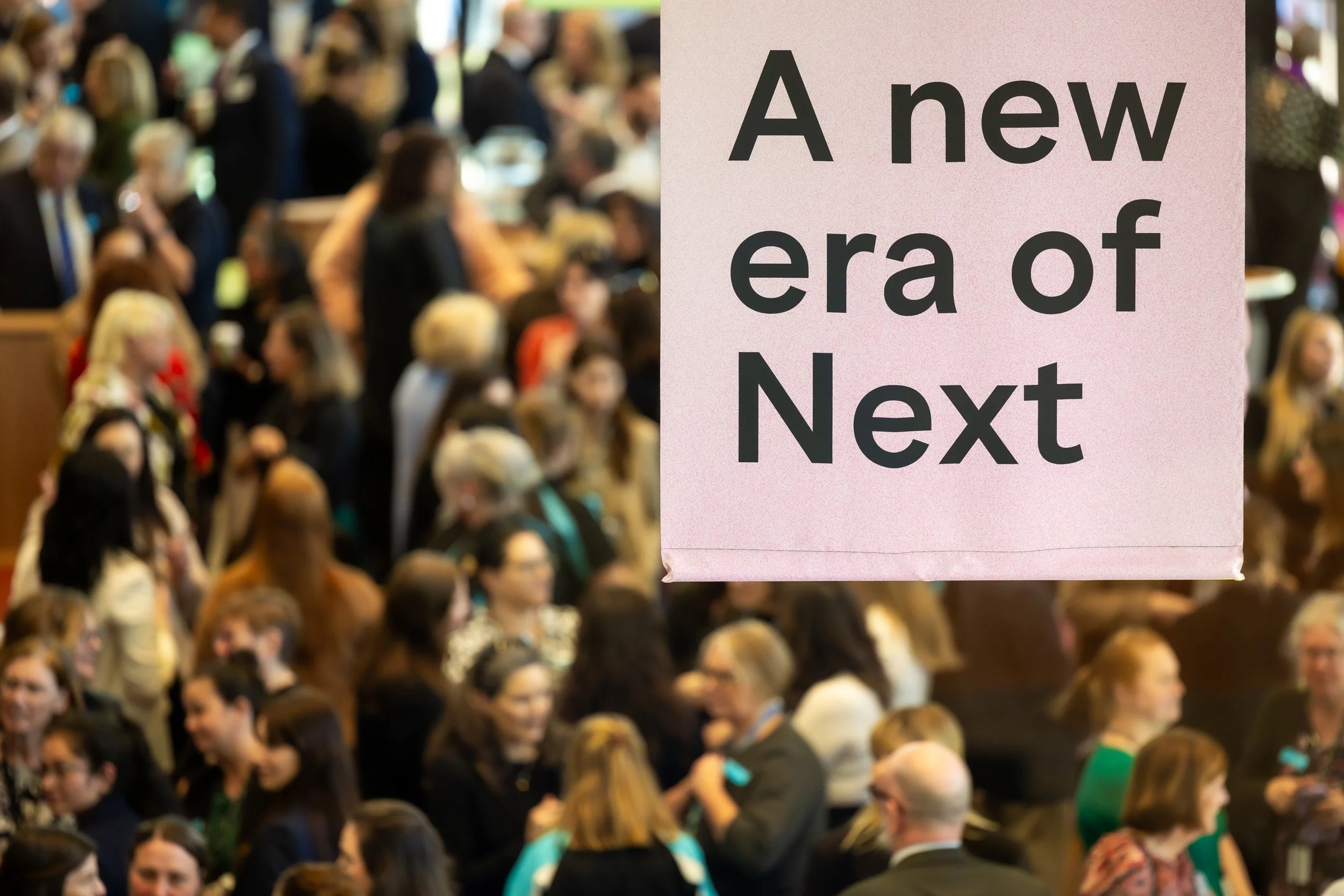 The bottom of a pink "A new era of Next" banner hangs while in the background a crowd of people are mingling.