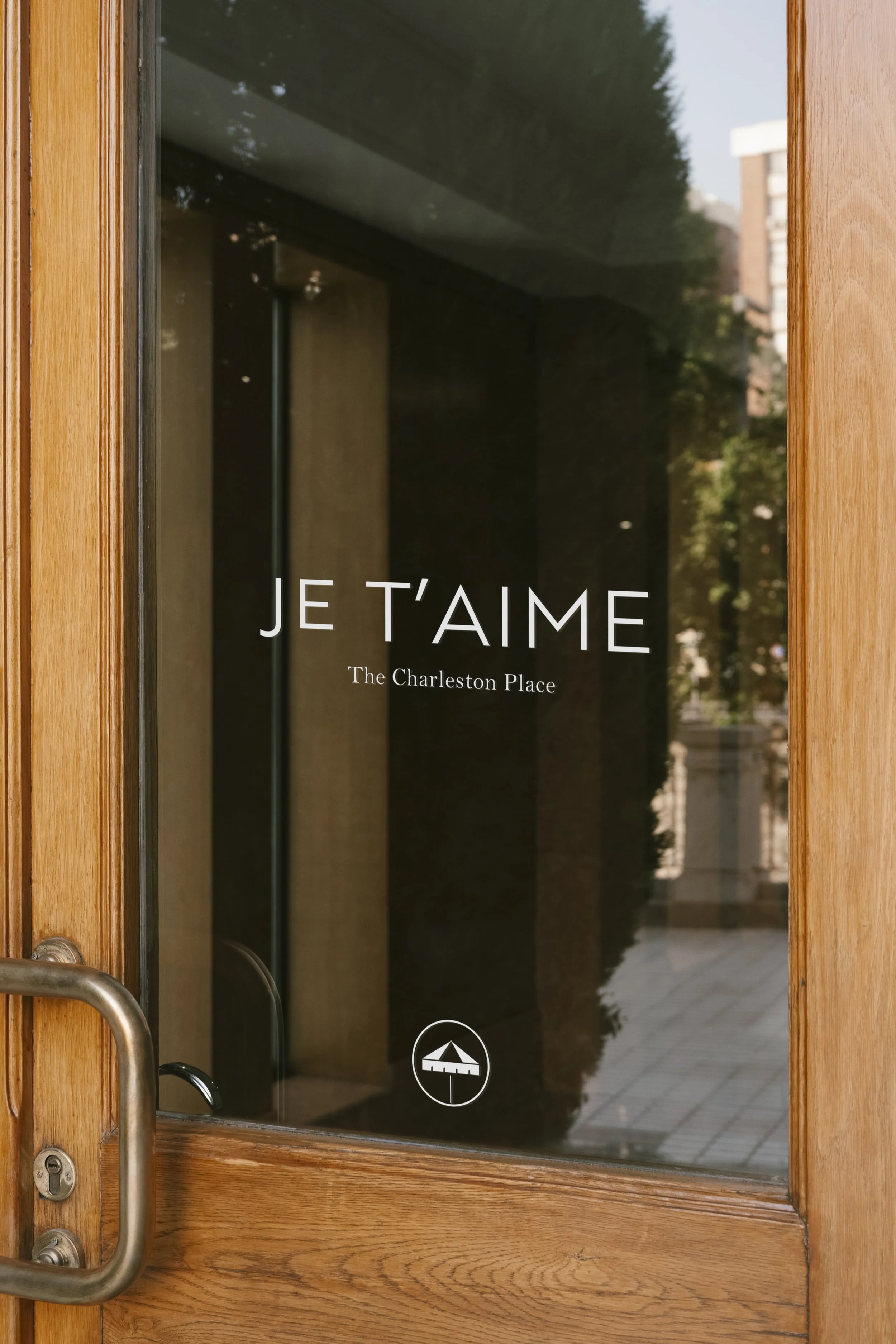 Door with glass window reading 'Je T'aime The Charleston Place' and a small umbrella logo at the bottom.
