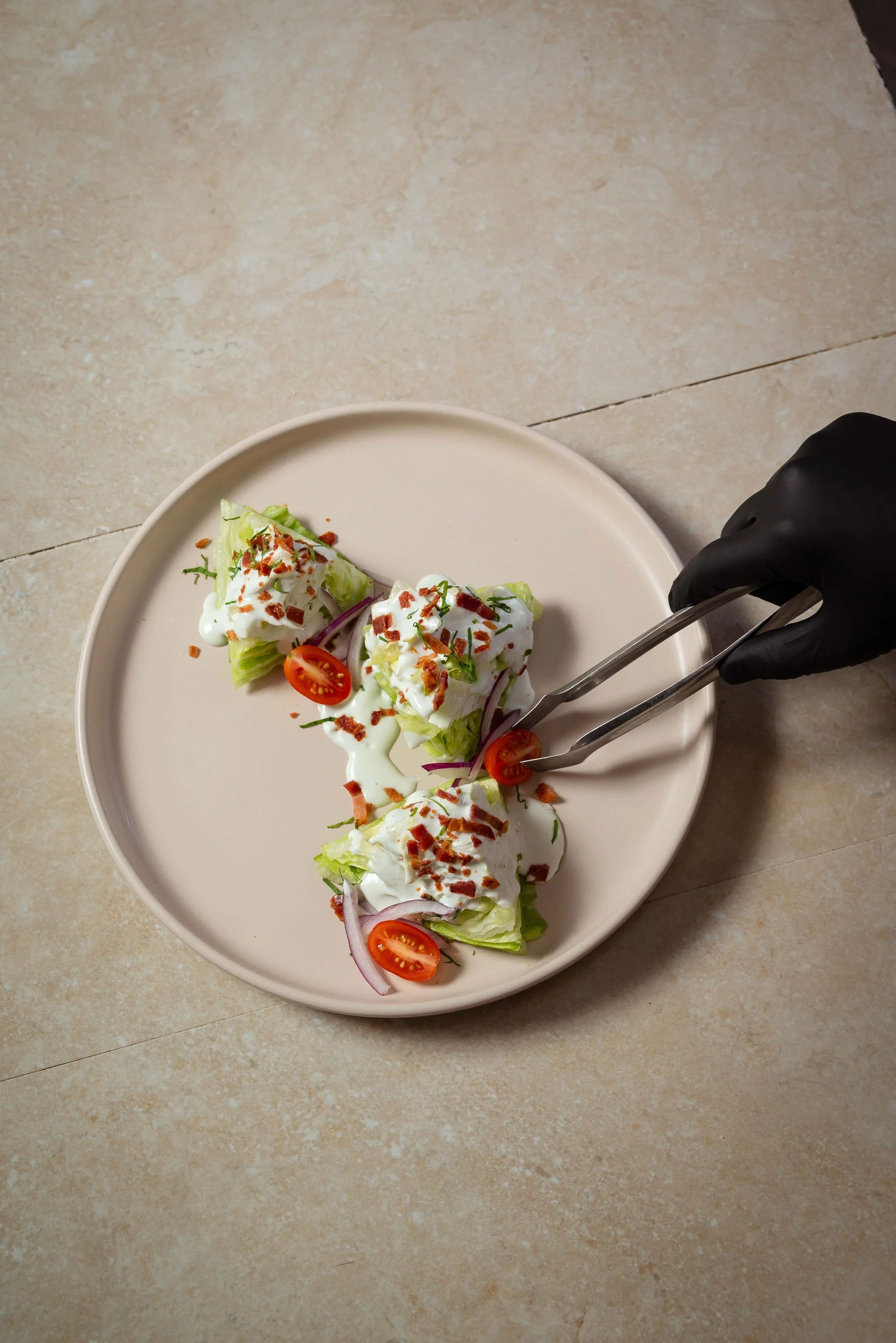 Tres rollitos de lechuga cubiertos con crema, tomates cherry, rodajas de cebolla, trocitos de tocino y hierbas en un plato beige.