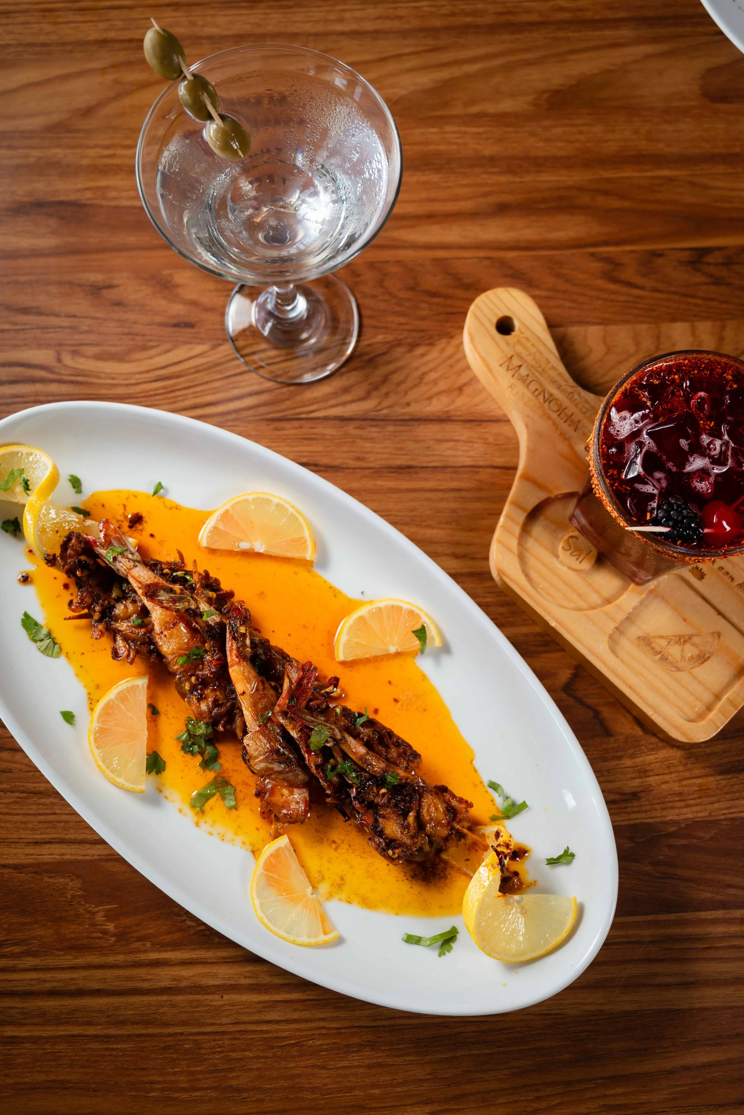 Camarones a la parrilla adornados con rodajas de limón y hierbas, con un acompañamiento de salsa naranja.