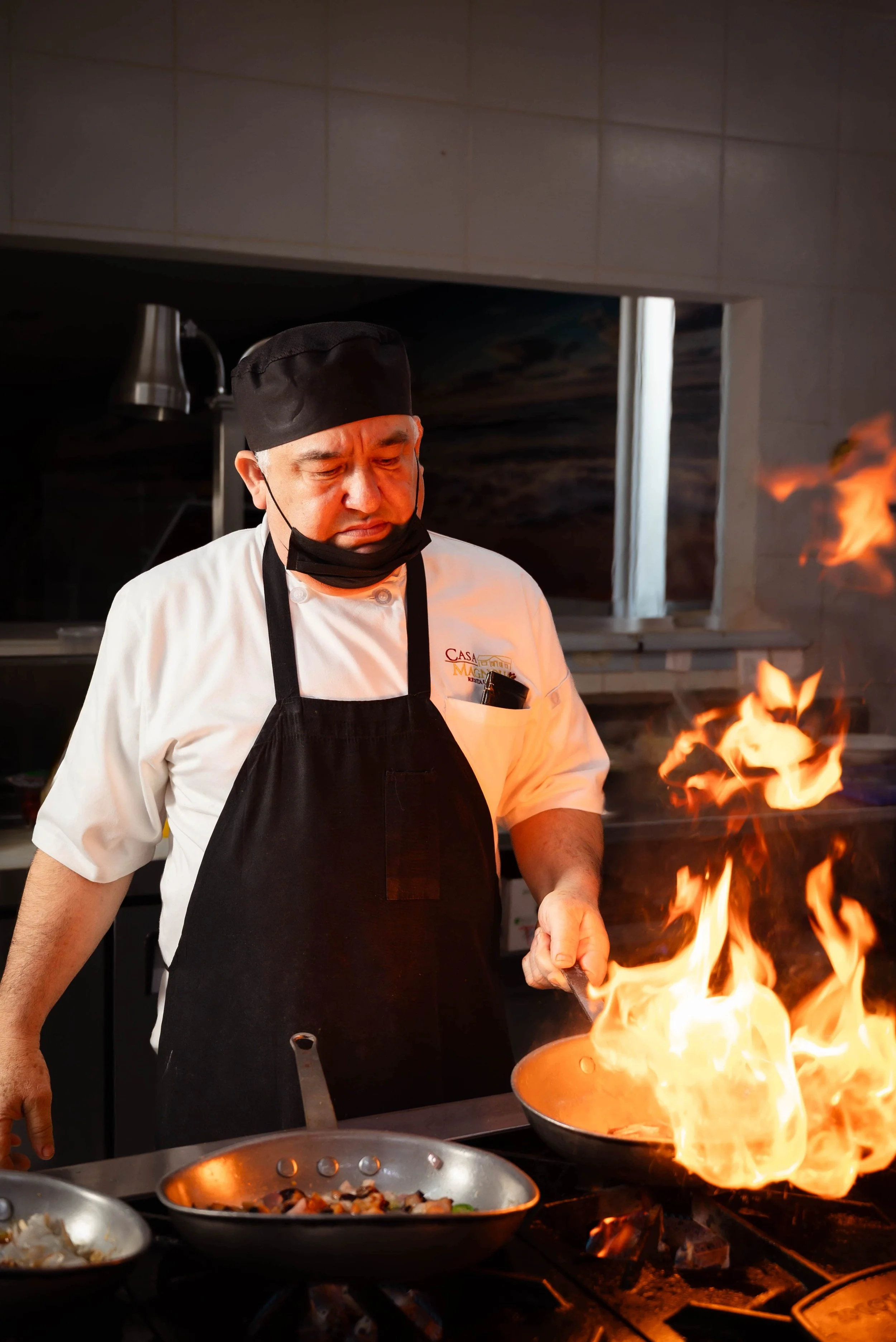 Chef cocinando en una cocina profesional con llamas saliendo de un sartén.
