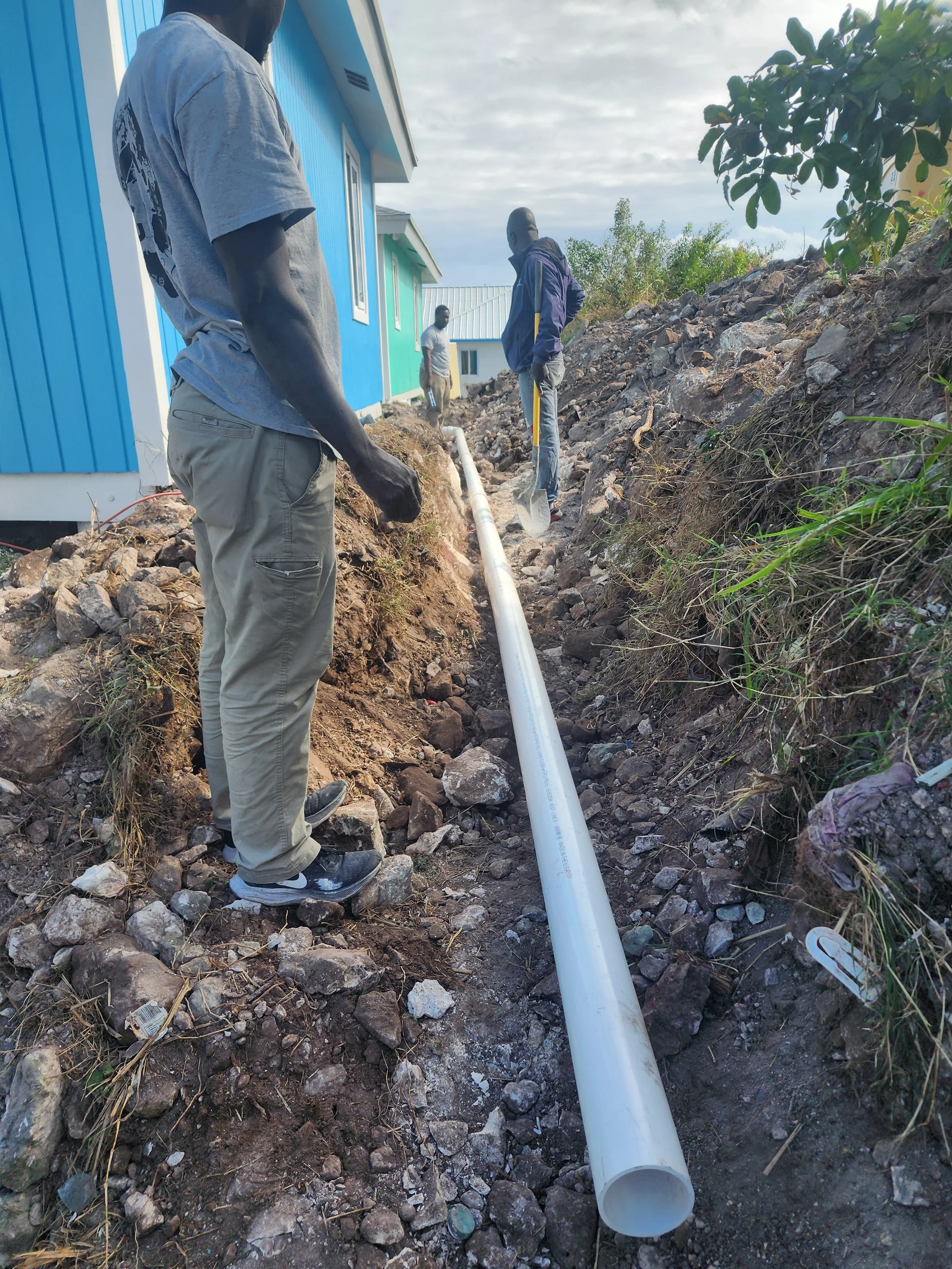 Men installing a large white pipe in a dug trench outside near colorful houses