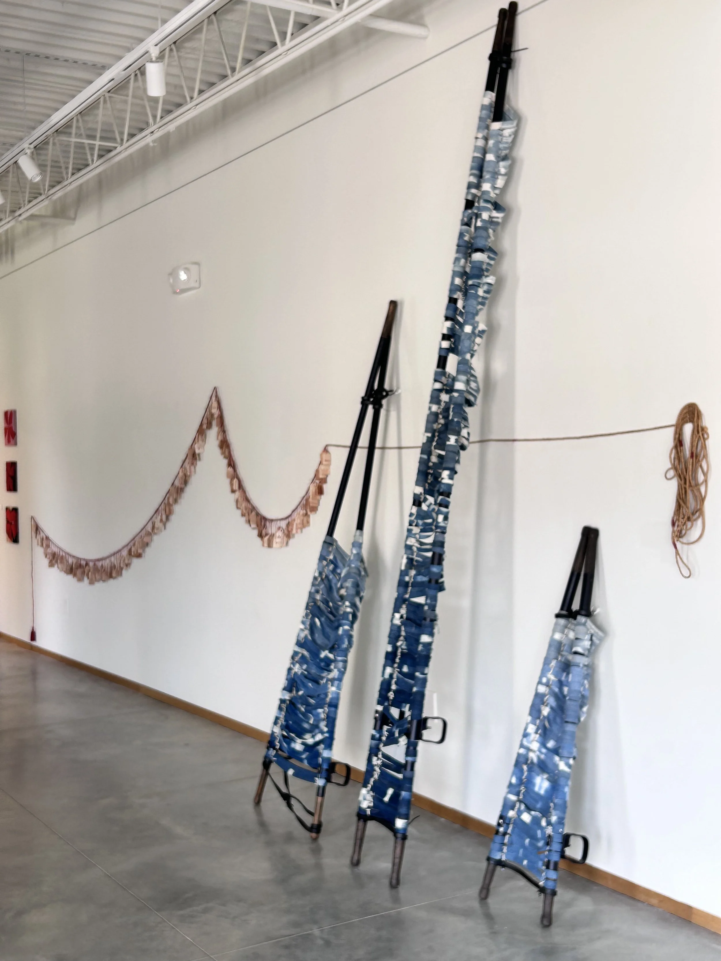 North wall: Breakfast of champions.
Tea bags, rope, cotton thread.
6 ft x 30 ft x 1 in; 2024.

Thoughts and Prayers.
Bleached denim, US military field stretchers, rubber.
8 ft x 18 ft x 3 ft; 2020.