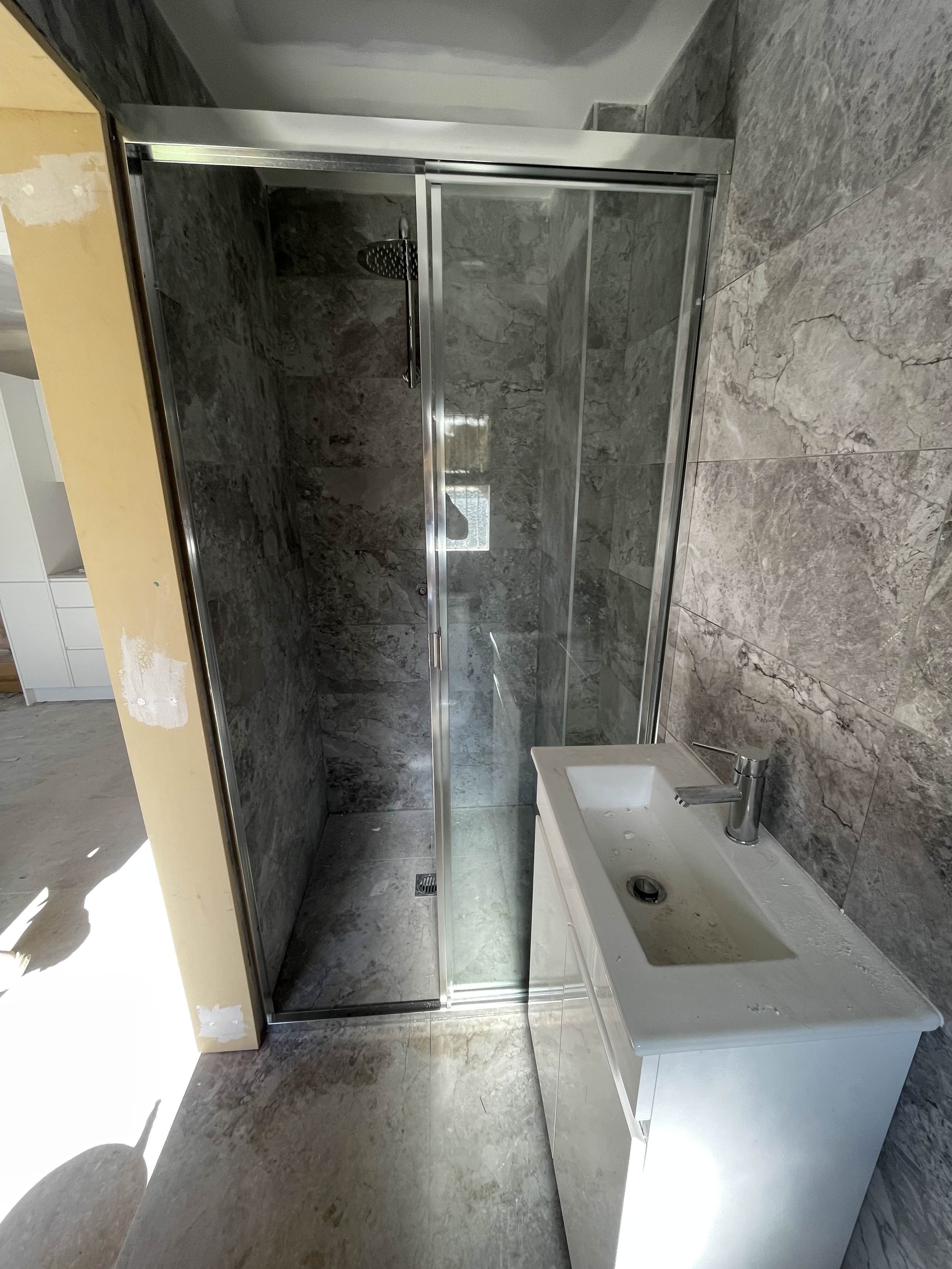 Bathroom with a glass shower enclosure with dark marbled tiles and a white cabinet sink with a single-handle faucet.