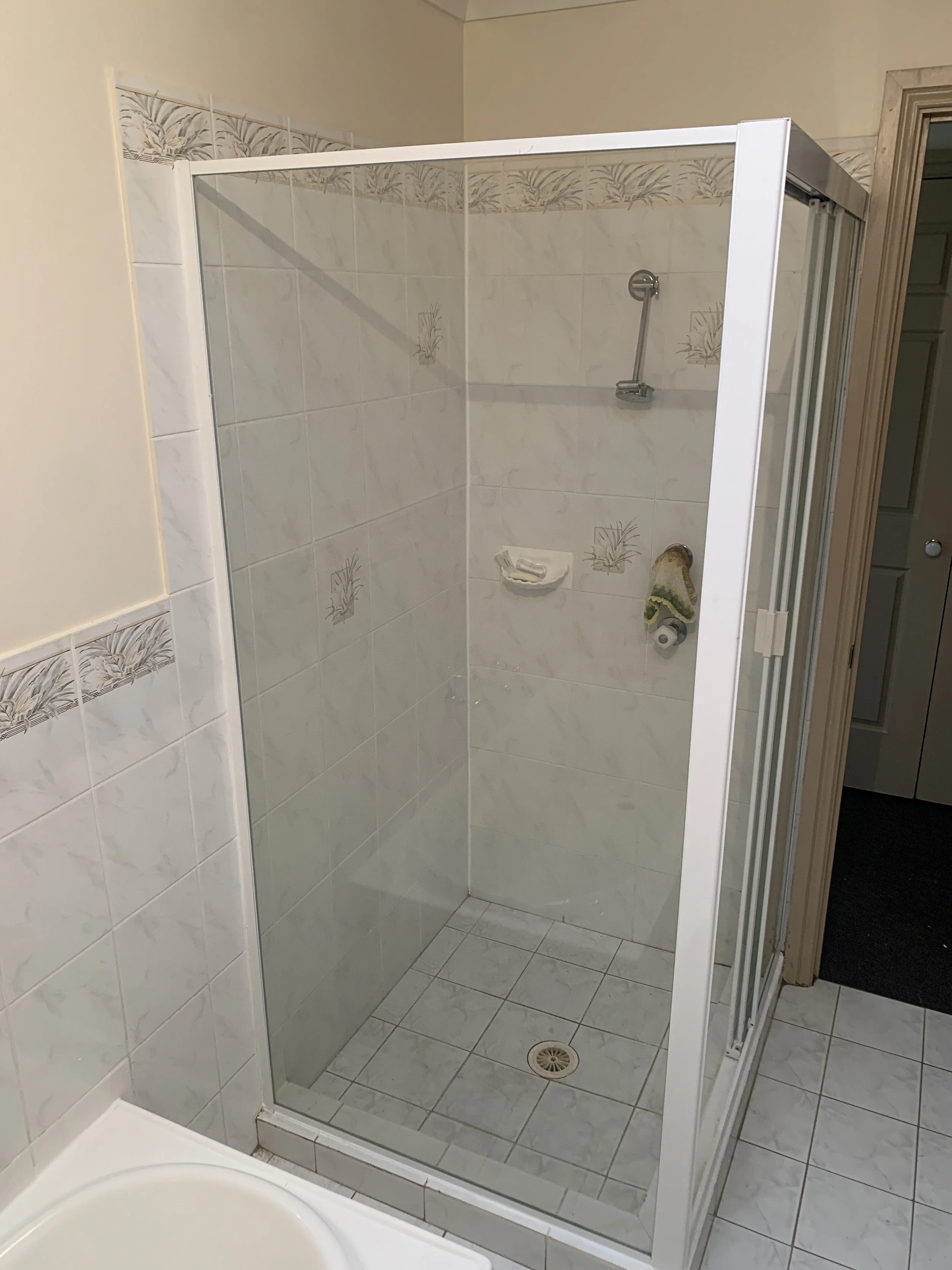 Bathroom with glass-enclosed shower, white tiles, and floral accents.