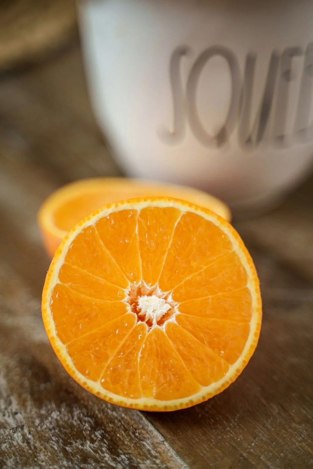 A halved orange on a wooden surface with a white mug in the background.