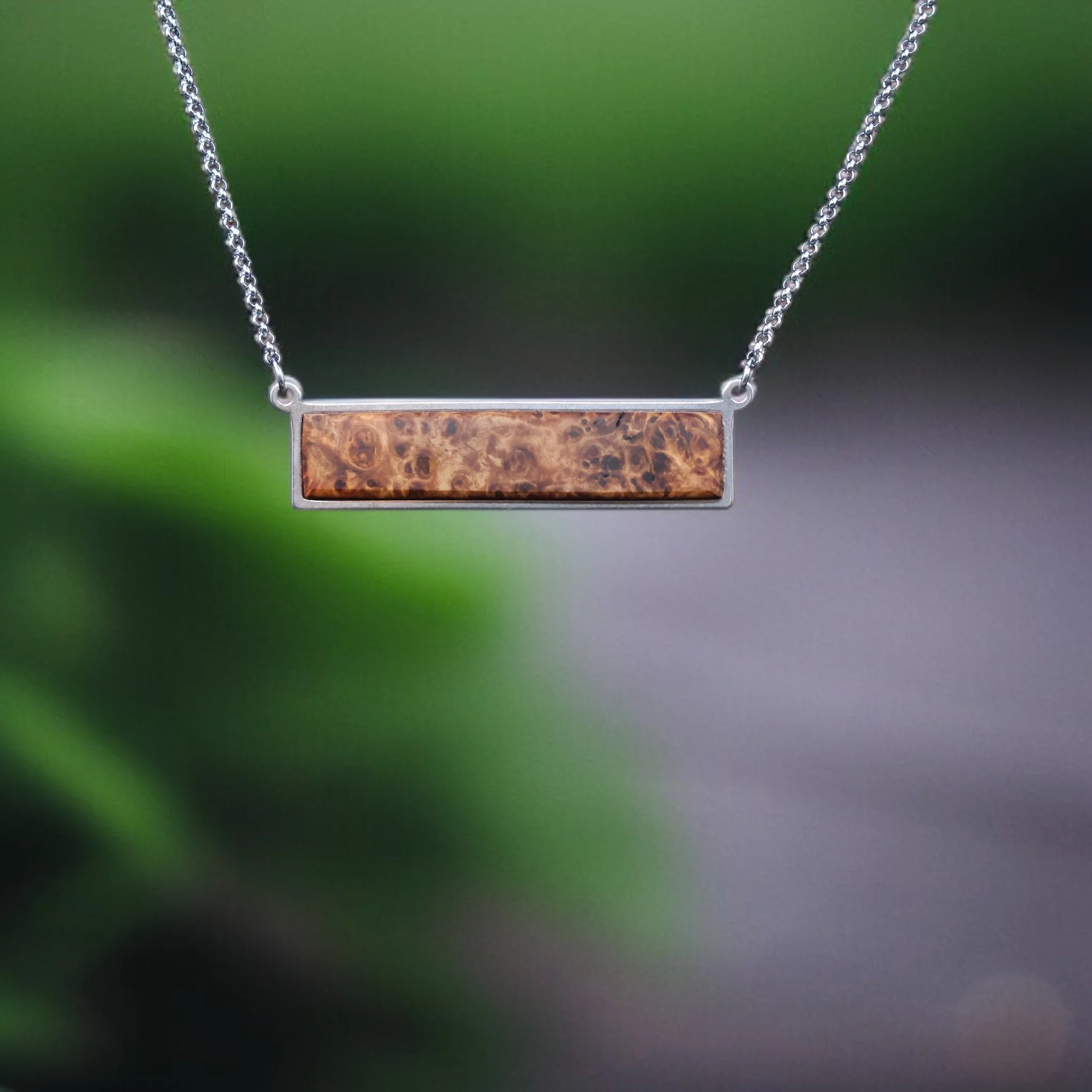 Wood and steel necklace floating with a green natural background showing its striking grain and minimalistic characteristics