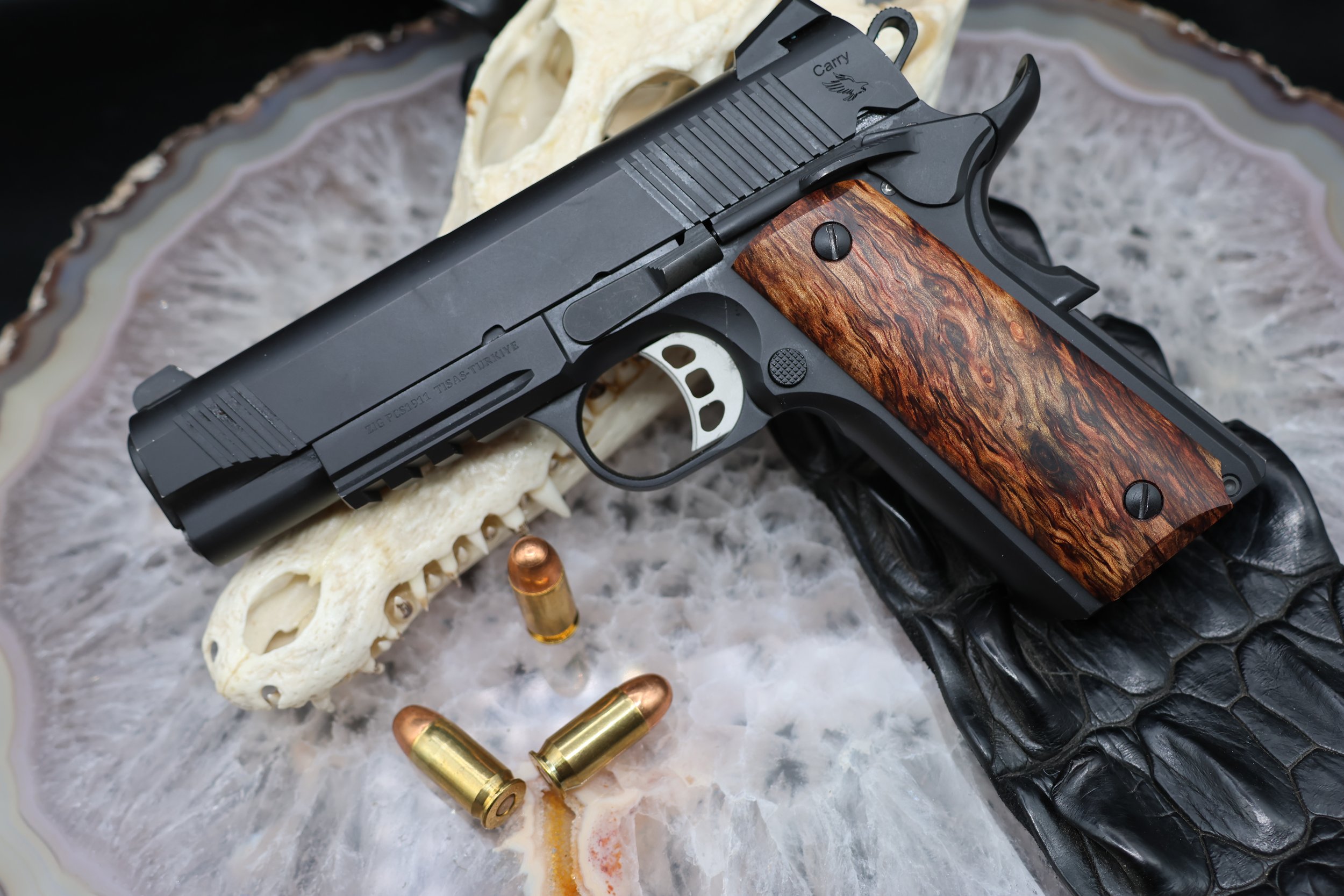Spalted Mango wood grip on black 1911 with silver trigger laying on top of crocodile hide and crocodile skull on top of agate slab with 40. cal bullets