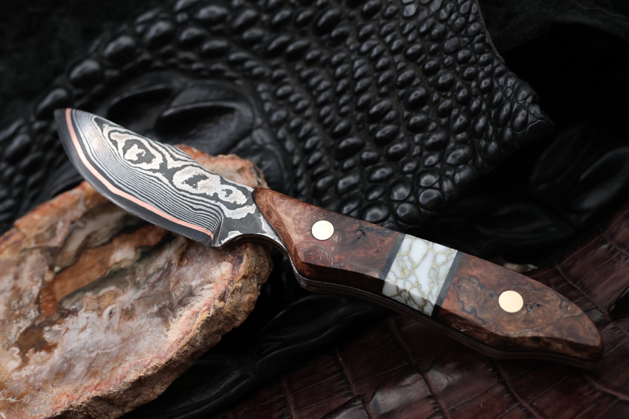 Damascus skinning blade set on stone slab over black crocodile hide