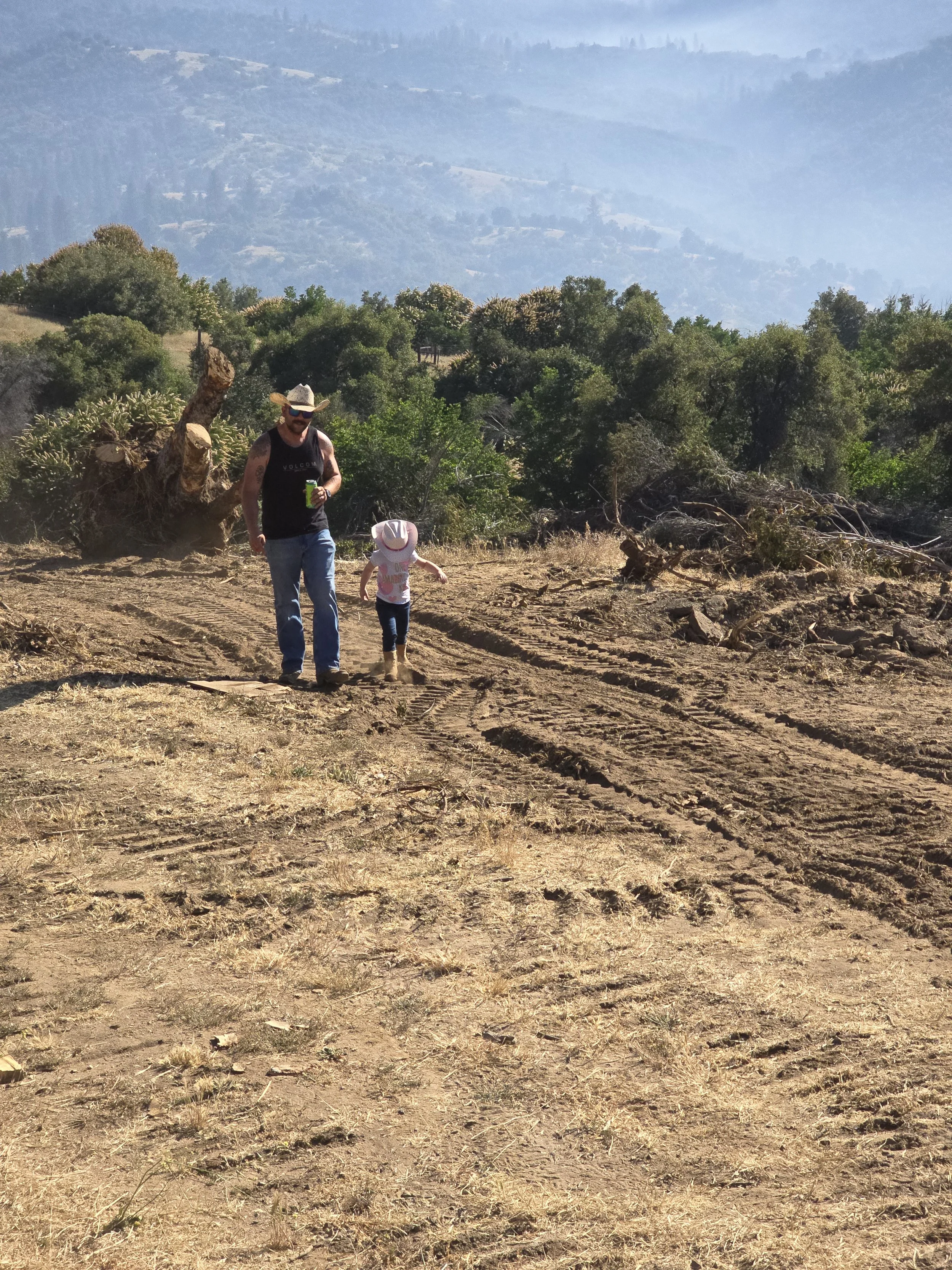 father and daughter in cowboy hats walking in the dirt with a forest and mountains behind them in the distance