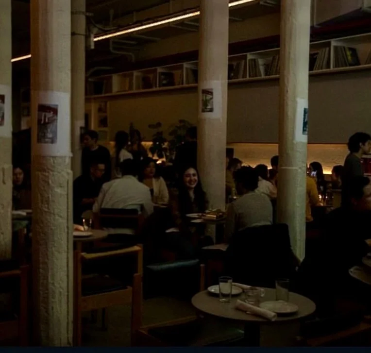 People dining in a dimly lit restaurant with wooden pillars and modern decor. MARIAM KVASHILAVA EXHIBITION