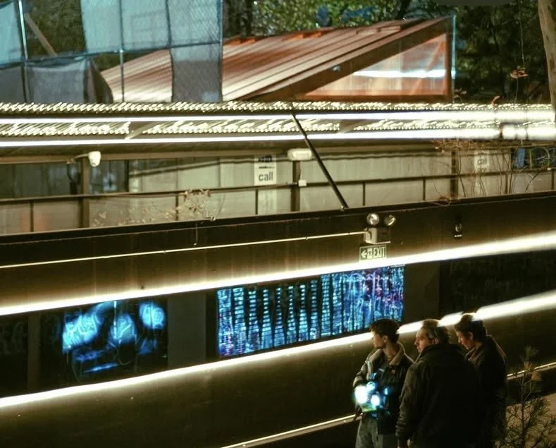 Three people standing outside a modern building with illuminated screens and neon lights at night.