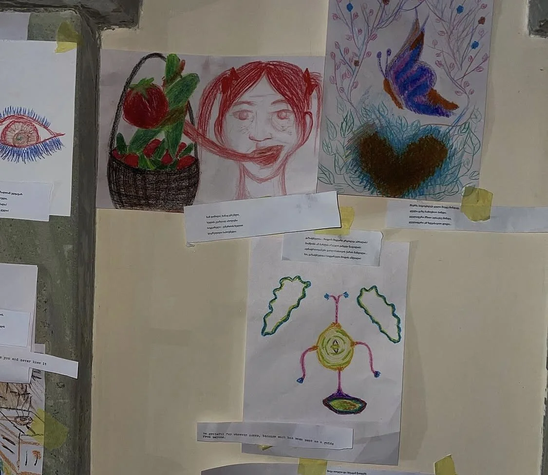 Collection of children's drawings taped to a wall, including a detailed eye, a strawberry basket with a face, a butterfly and heart, and a character with wings and a halo.