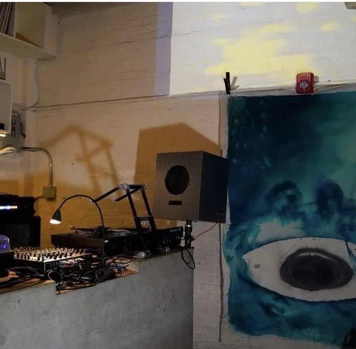Music DJ setup with turntable, mixer, and speaker in a room with a large eye mural on the wall.
