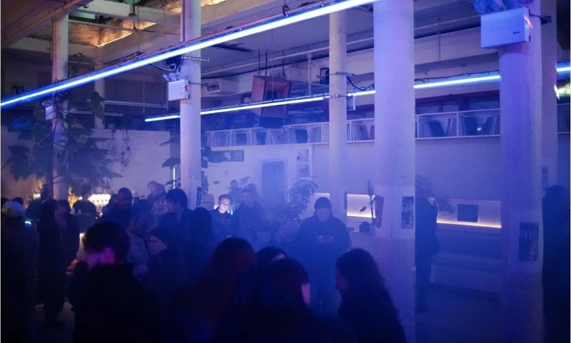 People dancing and socializing in a nightclub with blue neon lighting and smoke effects. MARIAM KVASHILAVA EXHIBITION