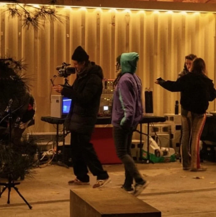 Group of people dancing indoors, with DJ equipment in the background, illuminated by warm yellow lighting.