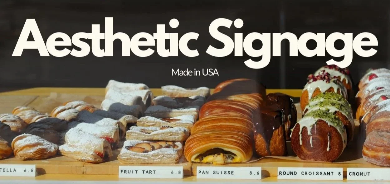 Display of various pastries including croissants, fruit tarts, a Swiss roll, and cinnamon rolls on a wooden board with labels and prices.