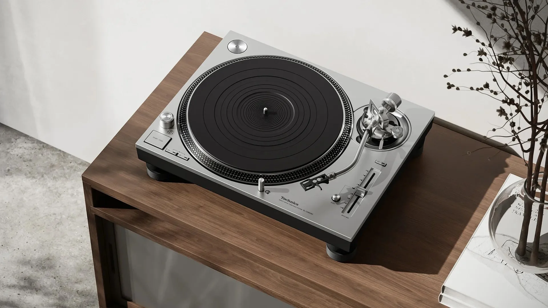 A Technics turntable on a wooden table with a book and a potted plant nearby.