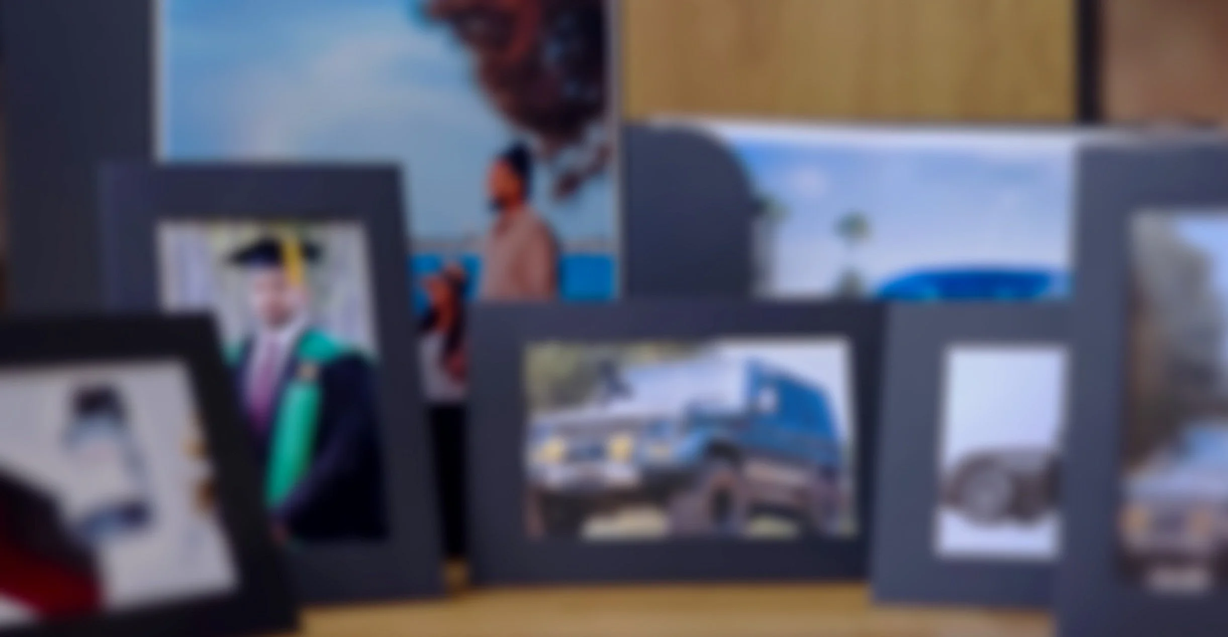 A blurred display of multiple framed photographs, including a graduation portrait and beach scenes.
