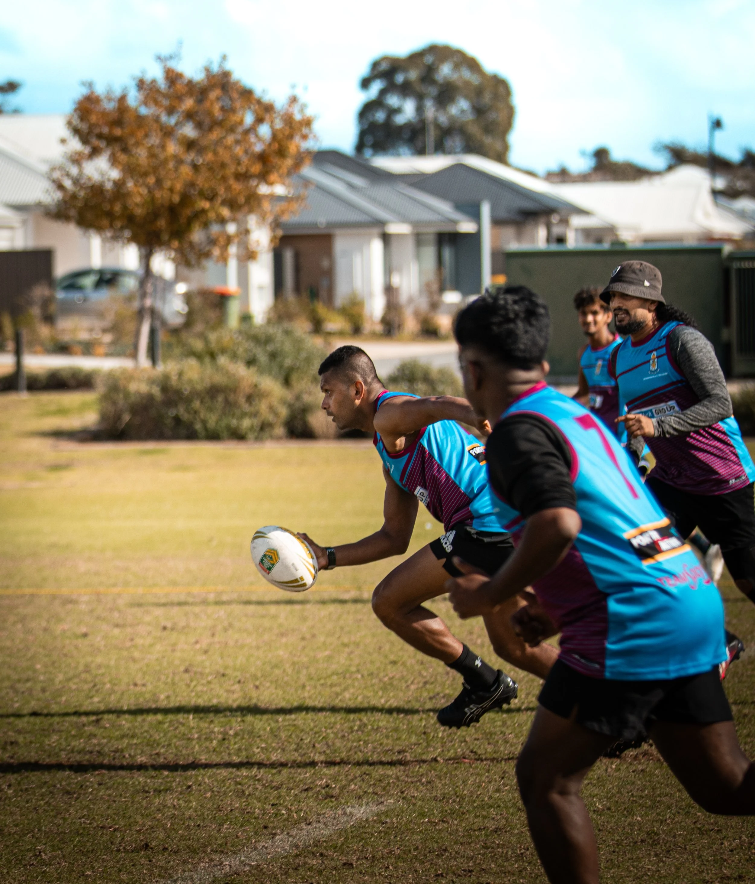 A group of rugby players in blue and purple uniforms running on a grassy field during a game.